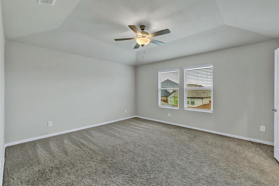 This room features a tray ceiling with a ceiling fan, two windows with blinds, and gray carpet