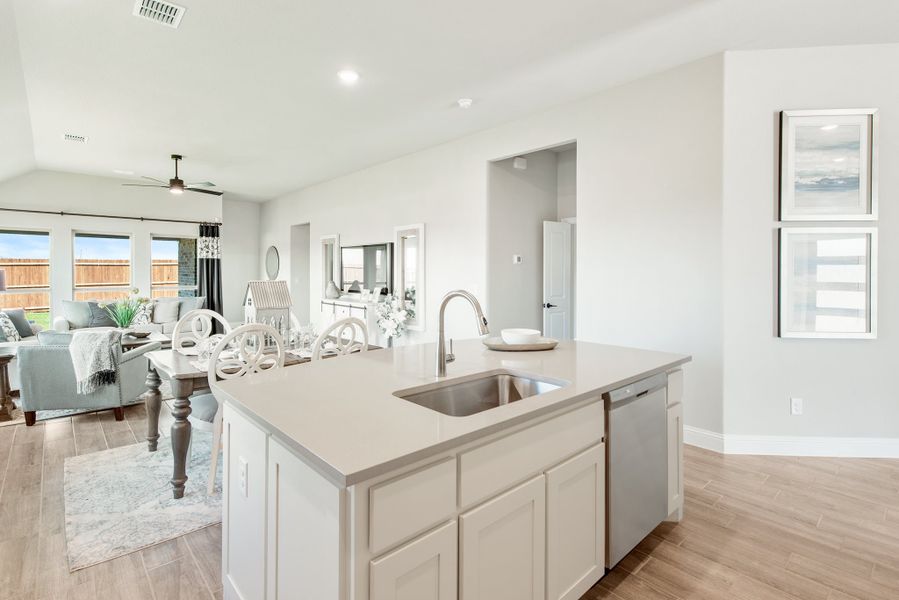 Kitchen island with white cabinets, undermount sink, and open view to dining and living areas with hardwood floors
