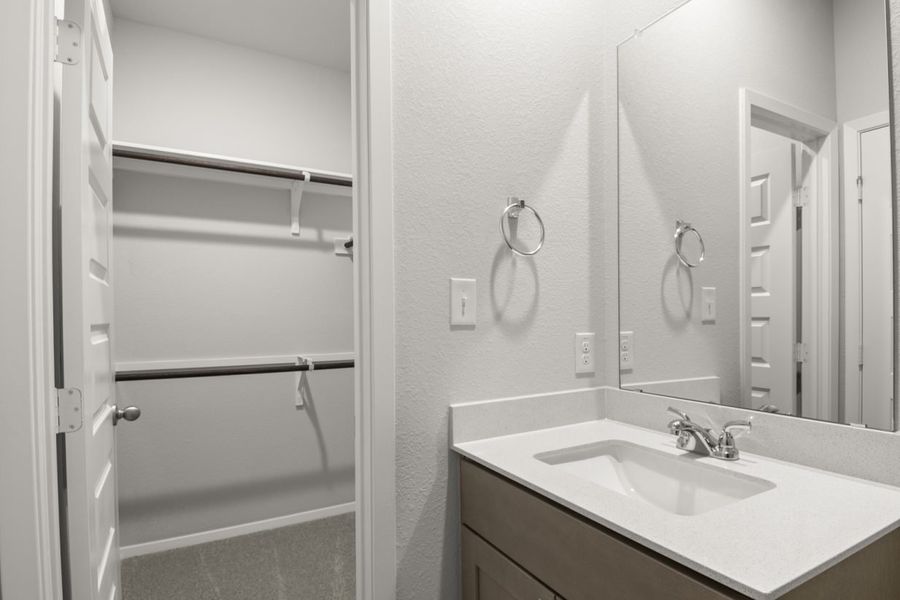 Image of a primary bathroom with a white vanity and mirror and a walk-in closet