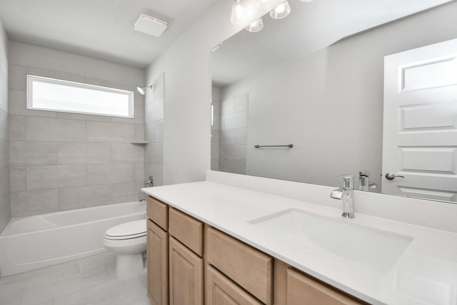 Secondary bath features tile flooring, bath/shower combo with tile surround, light stained wood cabinets, beautiful light countertop. Sample photo of completed home with similar floor plan. Actual colors and selections may vary.