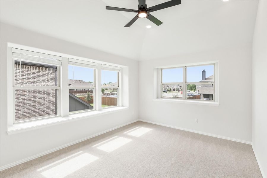 Empty bedroom with carpet, vaulted ceiling, ceiling fan, and multiple windows with neighborhood views