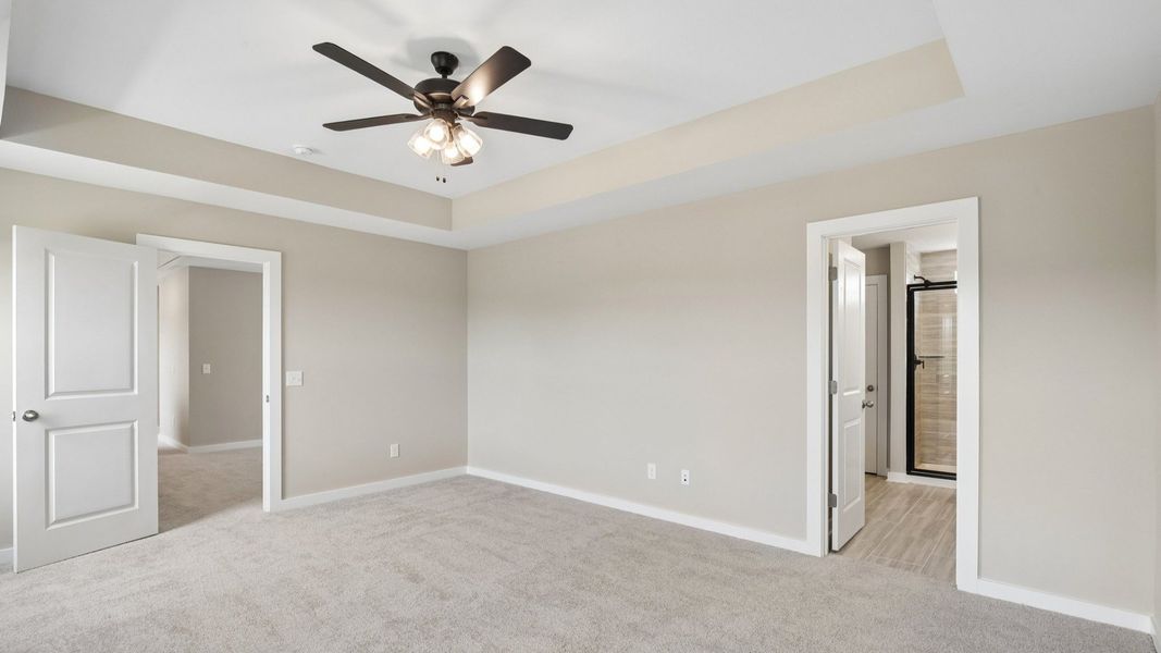 Bedroom with tray ceiling, windows, and entrance to primary bathroom Bedroom with tray ceiling, windows, and entrance to primary bathroom