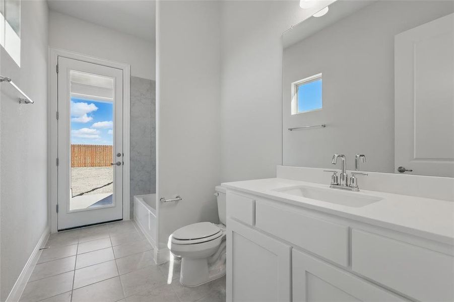 Bathroom with vanity, light tile patterned floors, and a tub to relax in