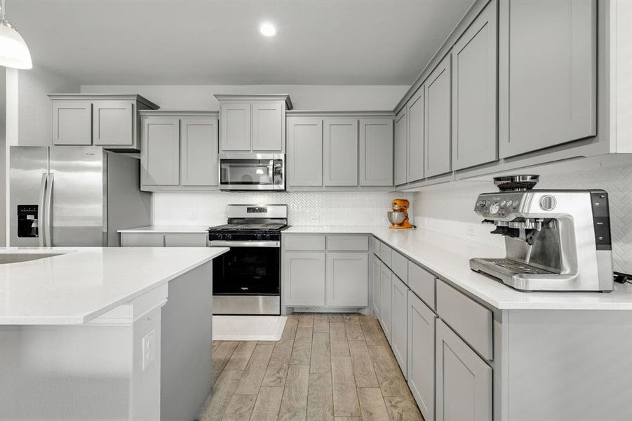 Kitchen with gray cabinetry, appliances with stainless steel finishes, light wood-style flooring, backsplash, and light countertops
