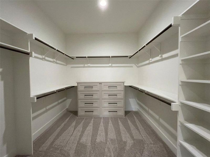 Spacious walk-in closet featuring built-in shelving, hanging rods, and a central dresser island with multiple drawers