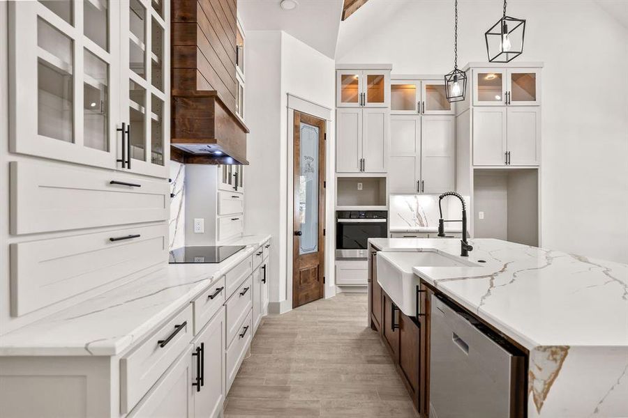 Kitchen featuring white cabinetry, glass insert cabinets, light stone countertops, appliances with stainless steel finishes, and an island with sink