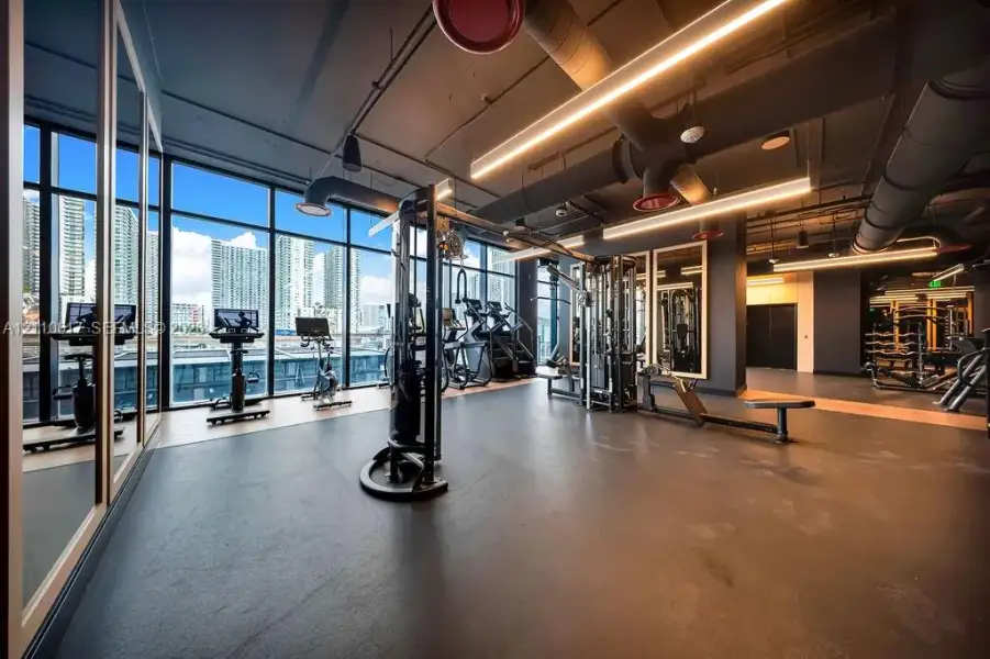 Fitness center featuring floor-to-ceiling windows, industrial-style exposed ductwork, recessed linear lighting, and wall-to-wall mirrors Fitness center featuring floor-to-ceiling windows, industrial-style exposed ductwork, recessed linear lighting, and wall-to-wall mirrors