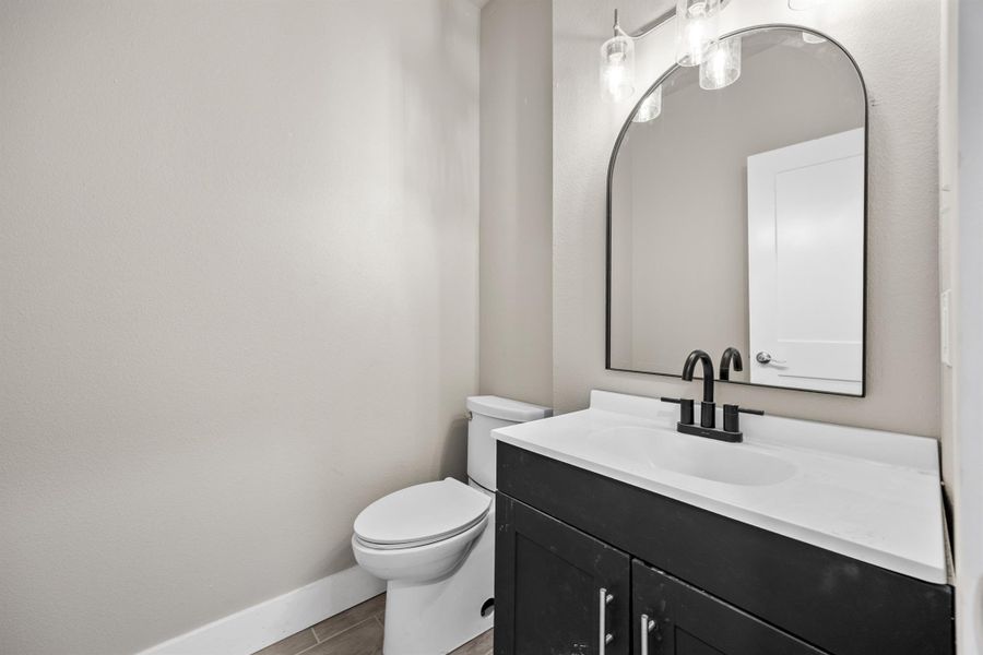 Half bathroom with toilet, wood finished floors, vanity, and baseboards Half bathroom with toilet, wood finished floors, vanity, and baseboards