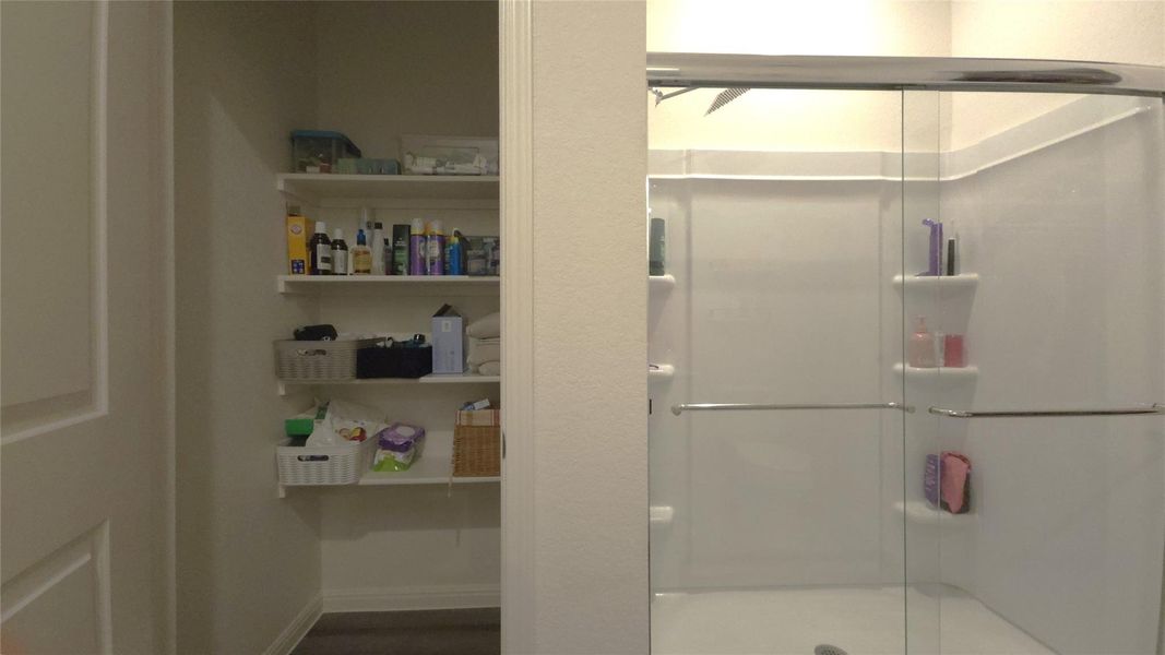 Enclosed shower with clear glass sliding doors and integrated shelving, accompanied by a dedicated linen closet featuring multiple open shelves