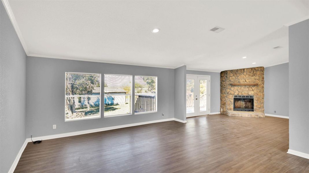 Unfurnished living room with french doors, dark wood-style flooring, a stone fireplace, and ornamental molding