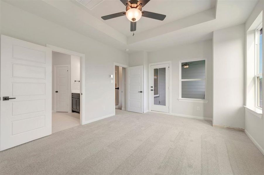 Spacious room featuring light-colored carpeting, a tray ceiling with a ceiling fan, and multiple windows Spacious room featuring light-colored carpeting, a tray ceiling with a ceiling fan, and multiple windows