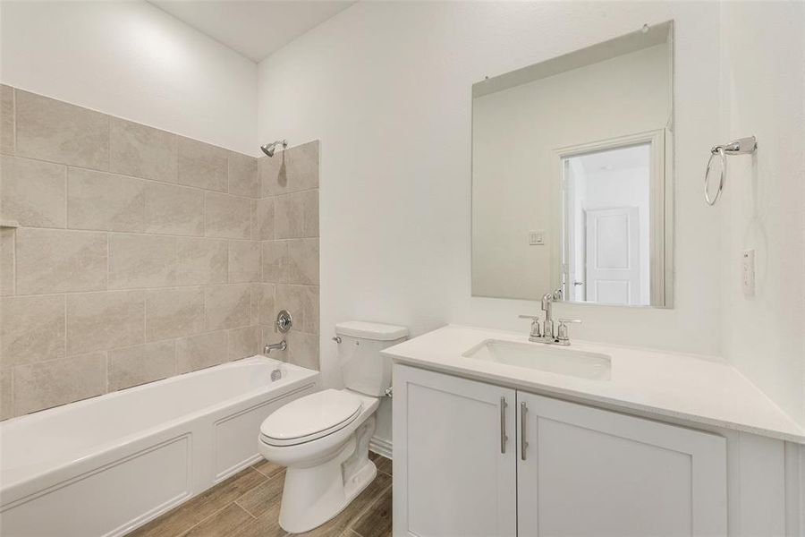 Full bathroom with vanity, hardwood / wood-style floors, tiled shower / bath, and toilet