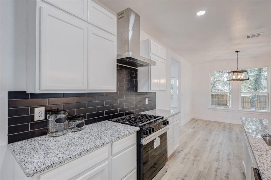 Kitchen featuring high end stove, light hardwood / wood-style floors, wall chimney range hood, and white cabinetry