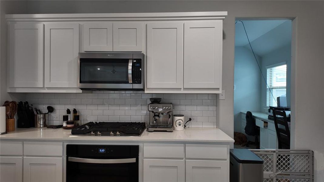 The kitchen features white shaker-style cabinetry, a subway tile backsplash, and stainless steel appliances including a microwave and an oven