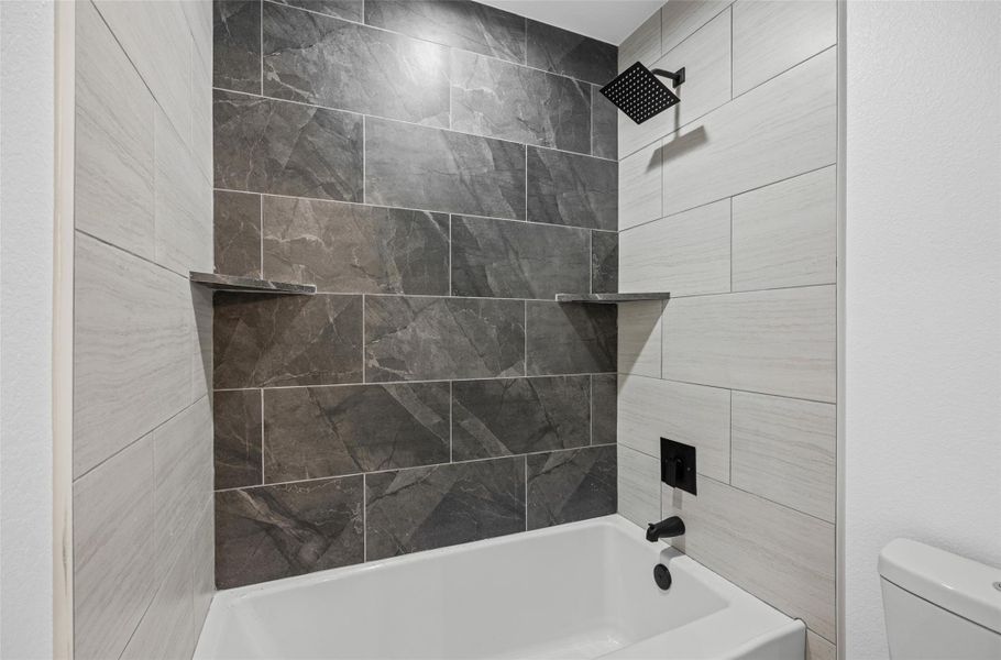 Bathtub with dark gray marble-look tile surround and contrasting light gray rectangular wall tiles Bathtub with dark gray marble-look tile surround and contrasting light gray rectangular wall tiles