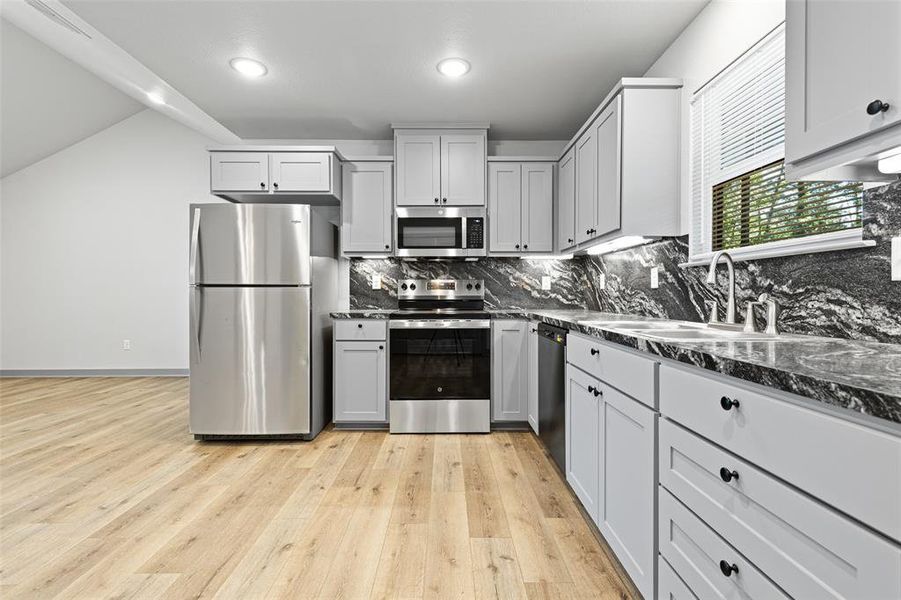 Kitchen with backsplash, appliances with stainless steel finishes, light wood-style flooring, gray cabinets, and recessed lighting Kitchen with backsplash, appliances with stainless steel finishes, light wood-style flooring, gray cabinets, and recessed lighting