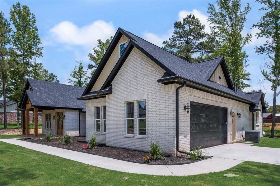White brick exterior featuring a dark asphalt shingle roof, black-framed windows, a covered front porch with wood columns, and an integrated garage with a dark door