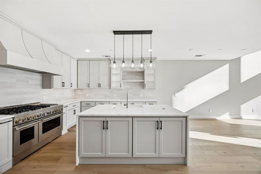 Kitchen with a center island with sink, range with two ovens, open shelves, light wood-type flooring, and light stone countertops Kitchen with a center island with sink, range with two ovens, open shelves, light wood-type flooring, and light stone countertops