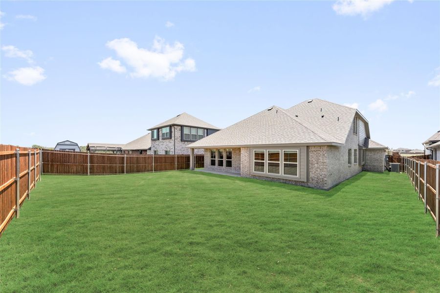 Brick home rear exterior with large fenced backyard, covered patio, and green lawn Brick home rear exterior with large fenced backyard, covered patio, and green lawn