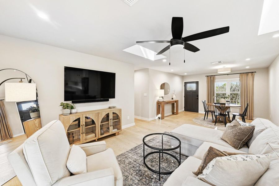 Living area with light wood-type flooring, a skylight, a ceiling fan, and recessed lighting