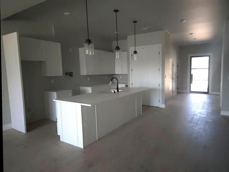 Kitchen featuring white cabinets, a kitchen island with sink, pendant lighting, and wood finished floors