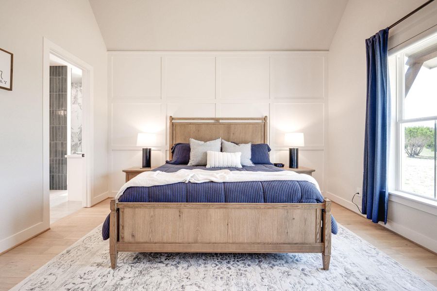 Bedroom featuring lofted ceiling, wood finished floors, a decorative wall, and connected bathroom