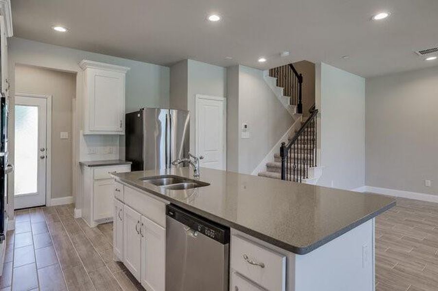 Kitchen with appliances with stainless steel finishes, a sink, light wood finished floors, an island with sink, and recessed lighting
