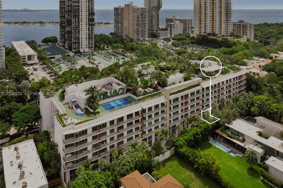 Aerial perspective of a multi-story residential building featuring a rooftop tennis court, landscaped terrace areas, and exterior balconies Aerial perspective of a multi-story residential building featuring a rooftop tennis court, landscaped terrace areas, and exterior balconies