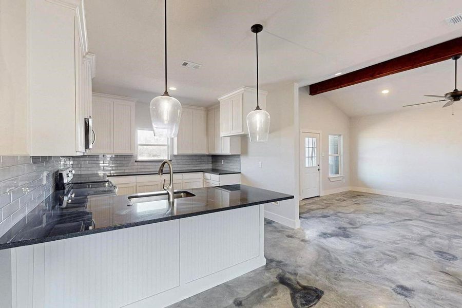 Kitchen with lofted ceiling with beams, a peninsula, a sink, appliances with stainless steel finishes, and tasteful backsplash