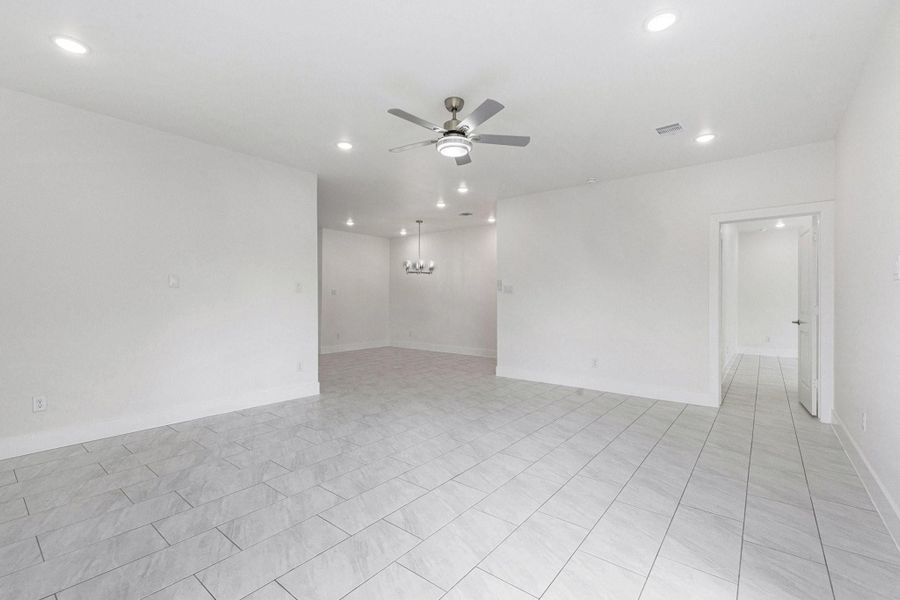 This photo features a spacious, open-concept room with light gray tile flooring and white walls. It includes recessed lighting, a ceiling fan, and a modern chandelier over the dining area. There's a doorway leading to another room, offering a versatile living space. This photo features a spacious, open-concept room with light gray tile flooring and white walls. It includes recessed lighting, a ceiling fan, and a modern chandelier over the dining area. There's a doorway leading to another room, offering a versatile living space.
