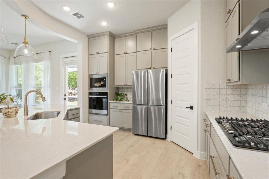 Kitchen featuring stainless steel appliances, gray cabinetry, light wood-type flooring, light stone countertops, undermount lighting, and pendant lighting