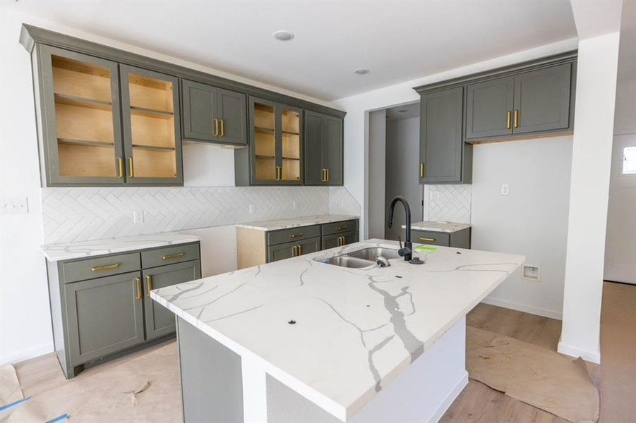 Kitchen with tasteful backsplash, an island with sink, light stone countertops, light wood-type flooring, and sink