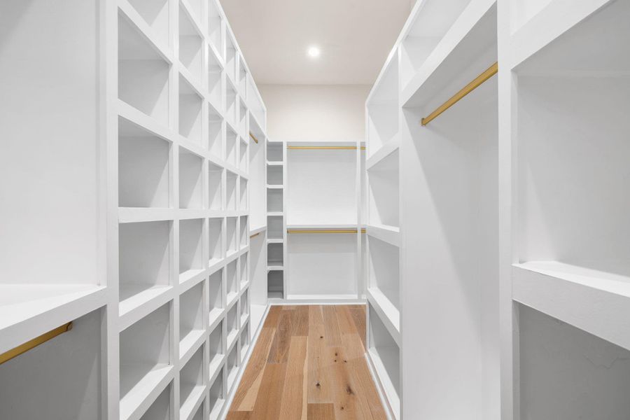 Custom closet system featuring extensive white shelving, multiple hanging rods, dedicated storage cubbies, and wood-finish flooring