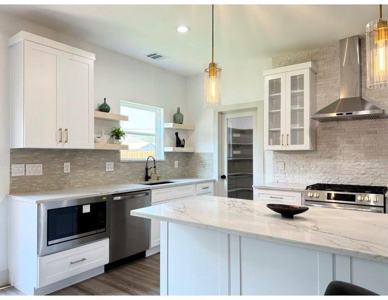 Kitchen featuring white cabinets, wall chimney range hood, decorative light fixtures, appliances with stainless steel finishes, and recessed lighting Kitchen featuring white cabinets, wall chimney range hood, decorative light fixtures, appliances with stainless steel finishes, and recessed lighting