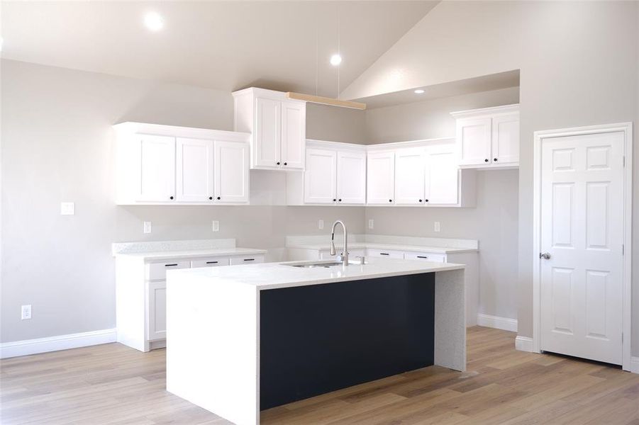 Kitchen featuring a kitchen island with sink, white cabinetry, light stone countertops, recessed lighting, and light wood-type flooring Kitchen featuring a kitchen island with sink, white cabinetry, light stone countertops, recessed lighting, and light wood-type flooring