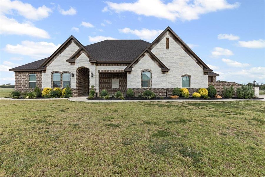 French country inspired facade featuring stone siding, a front lawn, and brick siding French country inspired facade featuring stone siding, a front lawn, and brick siding