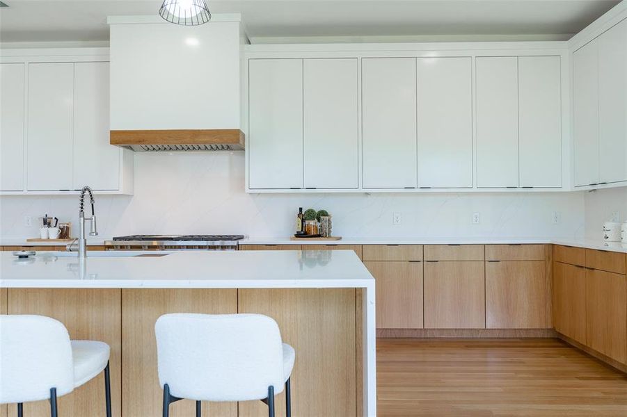 Kitchen with white cabinets, a breakfast bar area, light hardwood / wood-style floors, and premium range hood