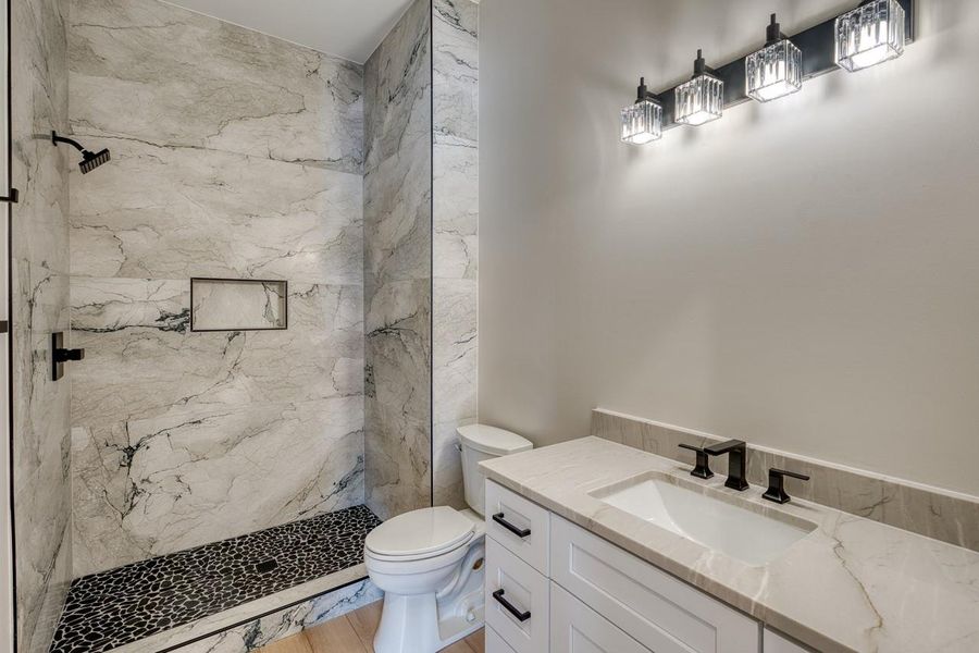 Luxurious marble-tiled shower with contrasting pebble flooring and a sleek vanity create a pristine bathroom retreat.