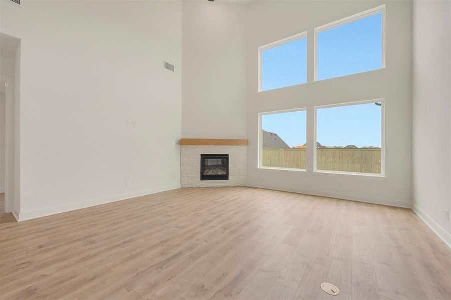 Spacious living area featuring a two-story ceiling, a contemporary fireplace with a light-toned stone surround and a wood mantel, and large windows providing ample natural light