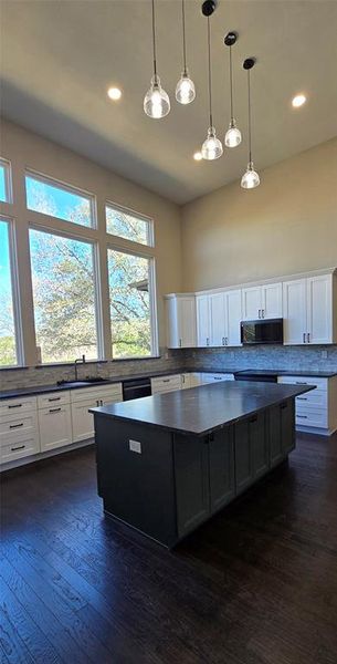 Kitchen featuring a center island, hanging light fixtures, stainless steel microwave, dark wood-style flooring, and dual tone cabinetry Kitchen featuring a center island, hanging light fixtures, stainless steel microwave, dark wood-style flooring, and dual tone cabinetry