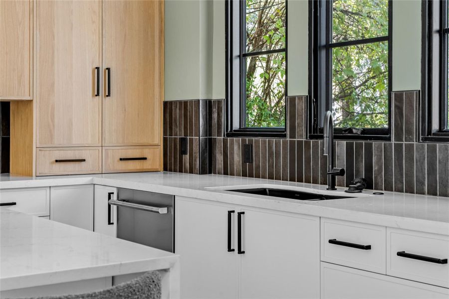 Kitchen featuring light stone countertops, light brown cabinets, modern cabinets, white cabinetry, and decorative backsplash