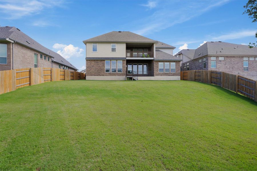 Back of property with a balcony, a fenced backyard, and brick siding Back of property with a balcony, a fenced backyard, and brick siding