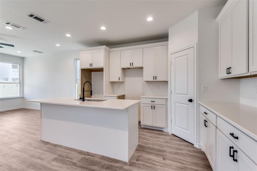 Kitchen with white cabinetry, sink, and an island with sink