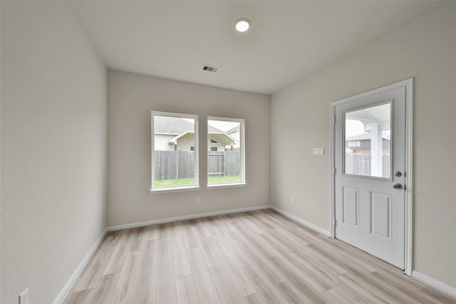 Bright room with light wood flooring, neutral walls, recessed lighting, and two large windows. It includes a door leading to a fenced backyard, offering ample natural light and outdoor access.