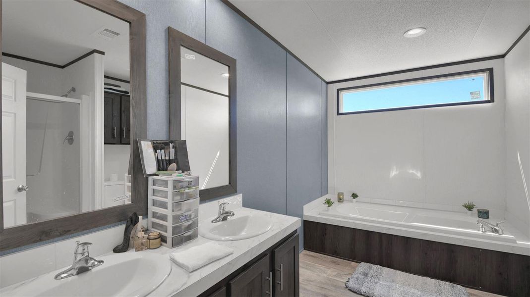 Bathroom with double vanity, a garden tub, a textured ceiling, a shower stall, and light wood-type flooring
