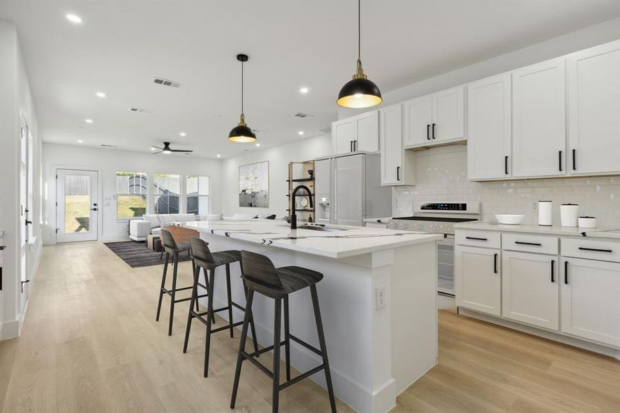 Kitchen with a center island with sink, white cabinetry, stove, sink, and decorative light fixtures