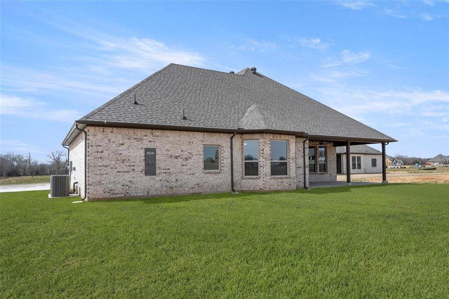 Back of property featuring roof with shingles, a yard, brick siding, and central AC Back of property featuring roof with shingles, a yard, brick siding, and central AC