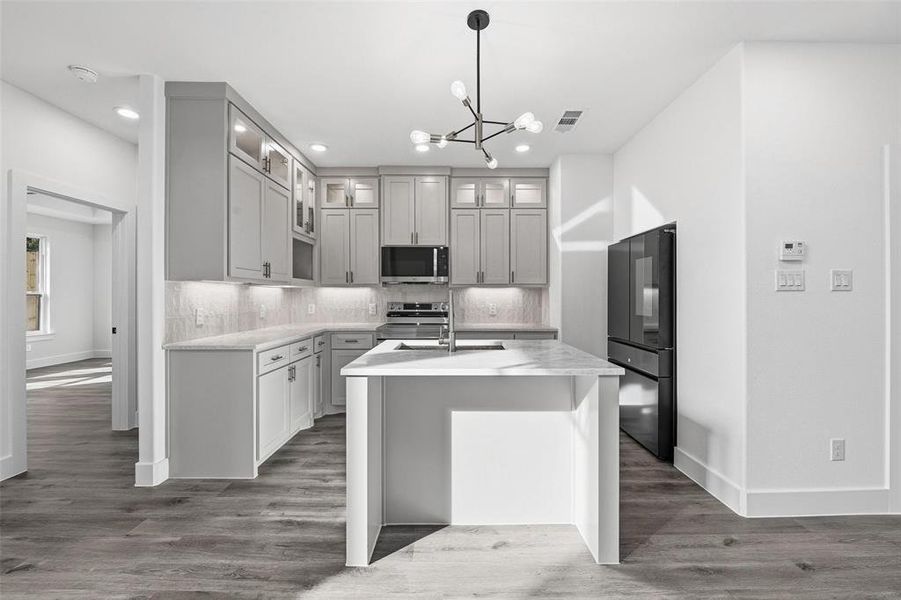 Kitchen featuring tasteful backsplash, a chandelier, dark wood finished floors, an island with sink, and appliances with stainless steel finishes