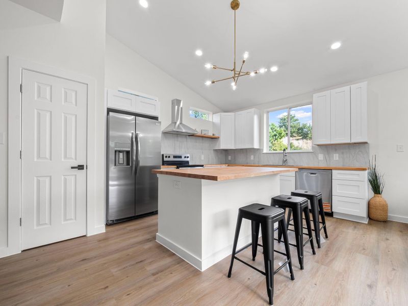 Contemporary kitchen featuring a central island with wood-finish countertop, white cabinetry, stainless steel appliances, and wood-finish flooring