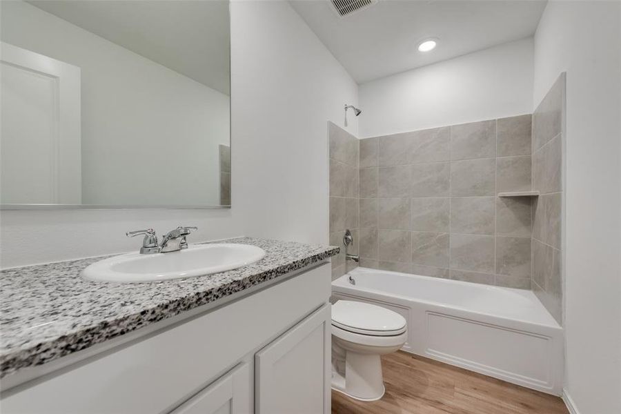 Full bathroom featuring hardwood / wood-style flooring, vanity, tiled shower / bath combo, and toilet